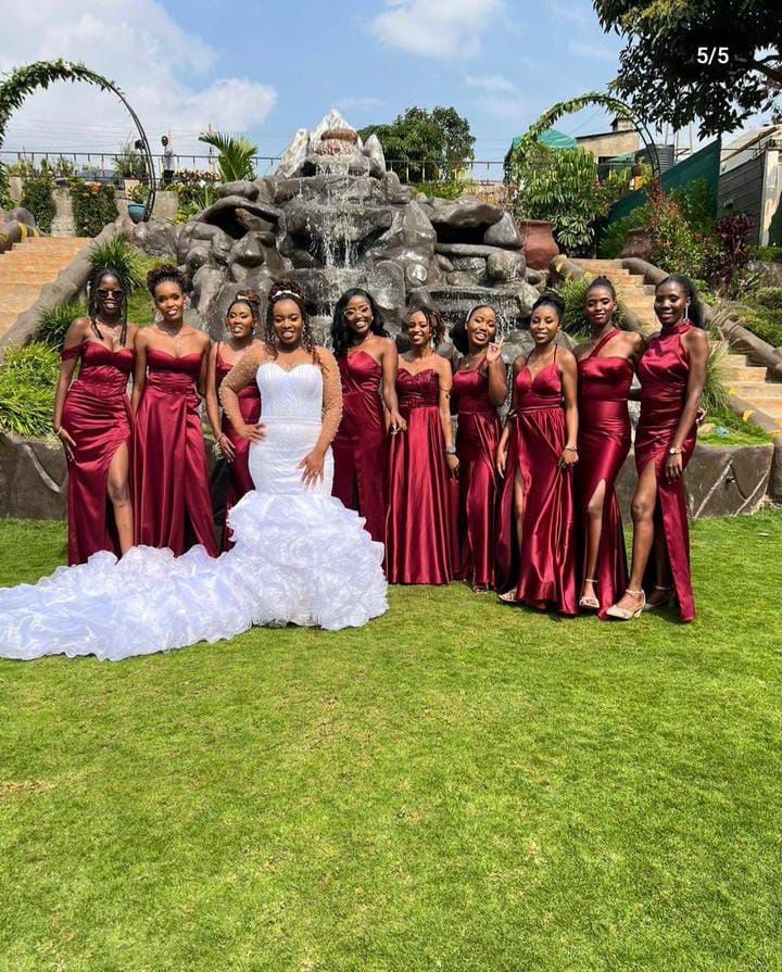 She's Confident bridal party, bride in an ivory mermaid gown with eight bridesmaids in deep red satin at a garden venue with stone fountain